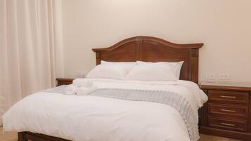 A neatly made bed with white bedding, a wooden headboard, and a bedside table with drawers.
