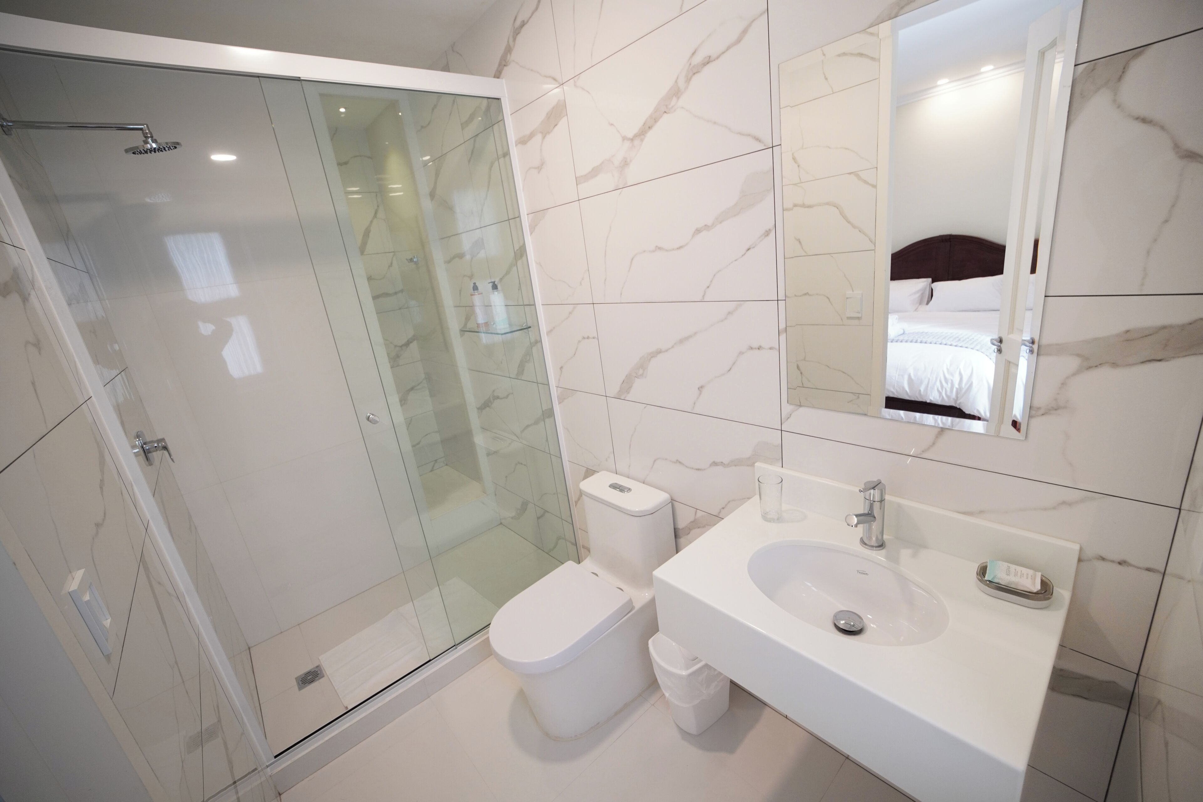 A modern bathroom with a glass-enclosed shower, a toilet, and a sink with a mirror above.