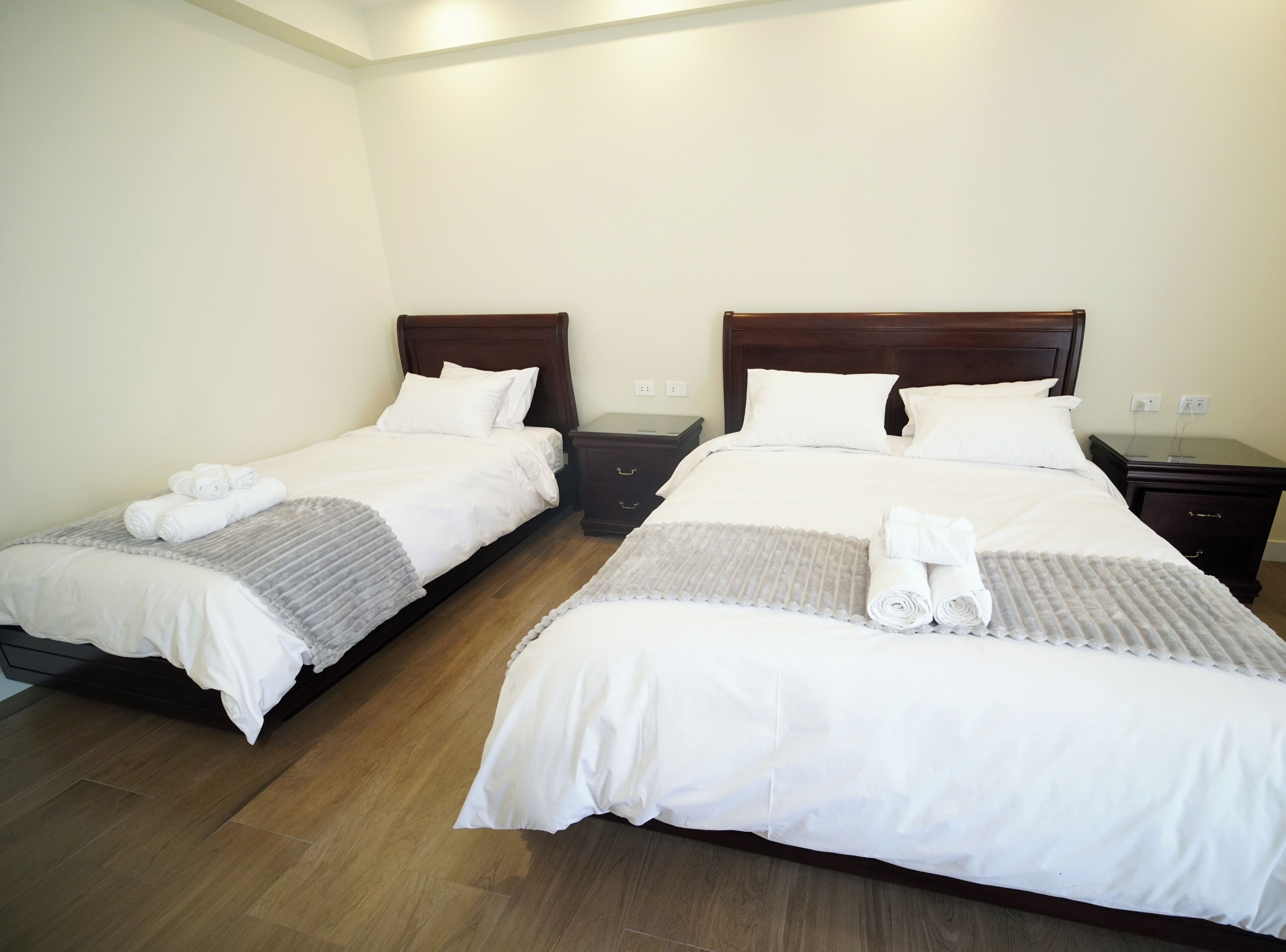 A hotel room with two single beds, each with a wooden headboard, white bedding, and rolled towels.