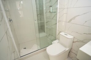 Un baño con ducha envuelta en vidrio, inodoro blanco y paredes con diseño de mármol.