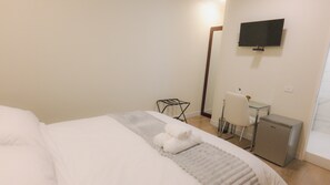 A hotel room with a bed, a desk with a chair, a television on the wall, and a small refrigerator. - Patrimonial Hotel Boutique (Cochabamba)