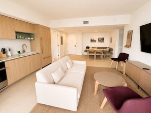A modern living room with a sofa, a coffee table, and a TV. There is a kitchen area with cabinets and a countertop. - Beautiful 2 Bed 2 Bath with balcony in Downtown (Miami)