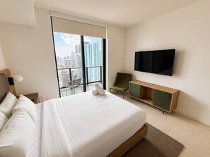 Een hotelkamer met een groot bed, een aan de muur bevestigde televisie, een stoel en uitzicht op de stad.