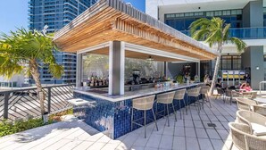 Ett utomhusområde med bar, en pergola av trä, en bardisk och sittplatser.