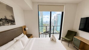 Ett hotellrum med en stor säng, en tv som är monterad på väggen, en balkong med utsikt över staden och en stol.