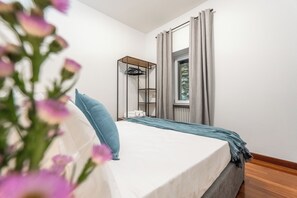 Un dormitorio con cama, una ventana con cortinas, estante de madera y perchero en la pared.