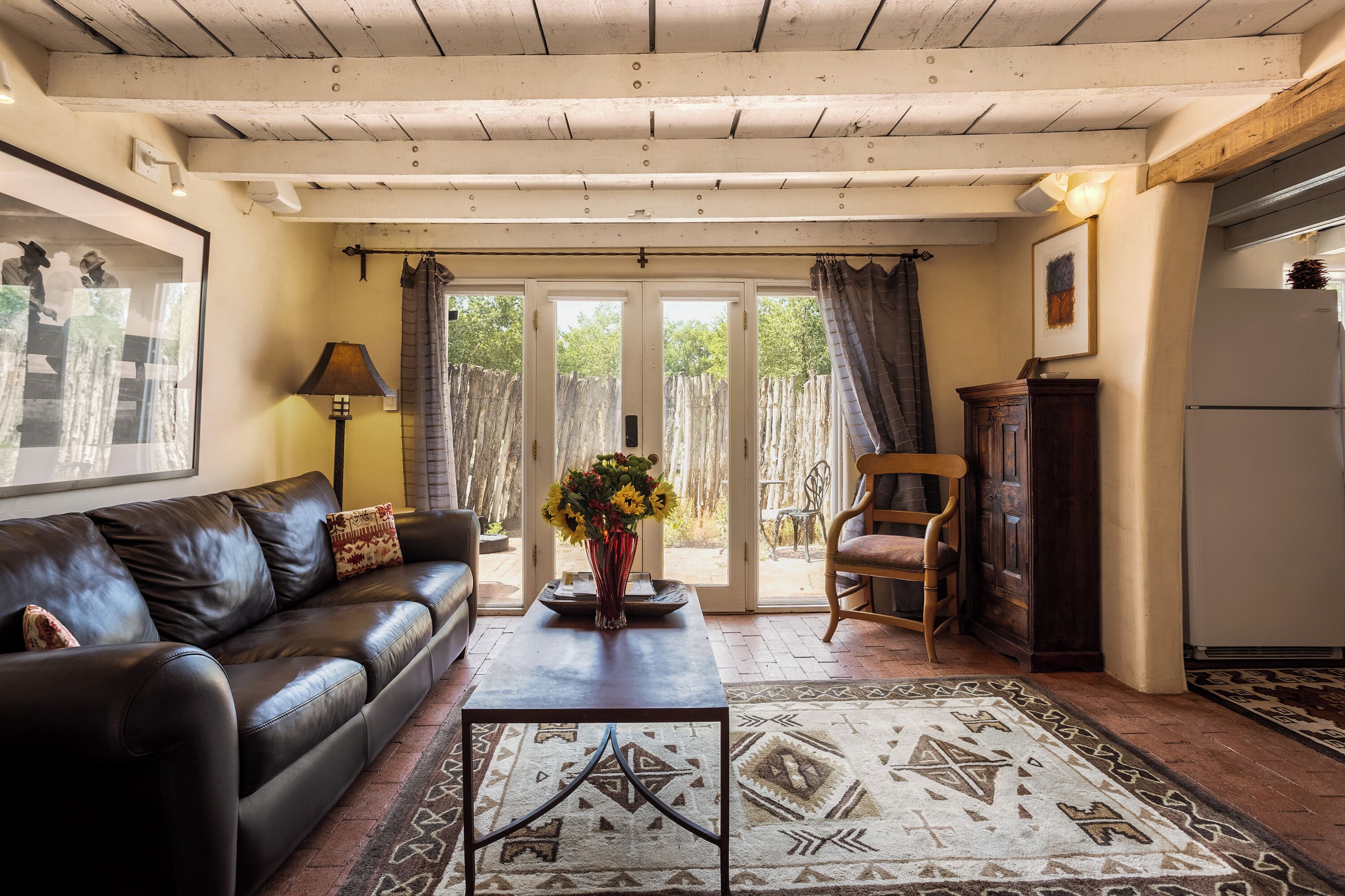 A living room with a leather sofa, a coffee table, a patterned rug, a wooden chair, and a door leading to an outdoor area.