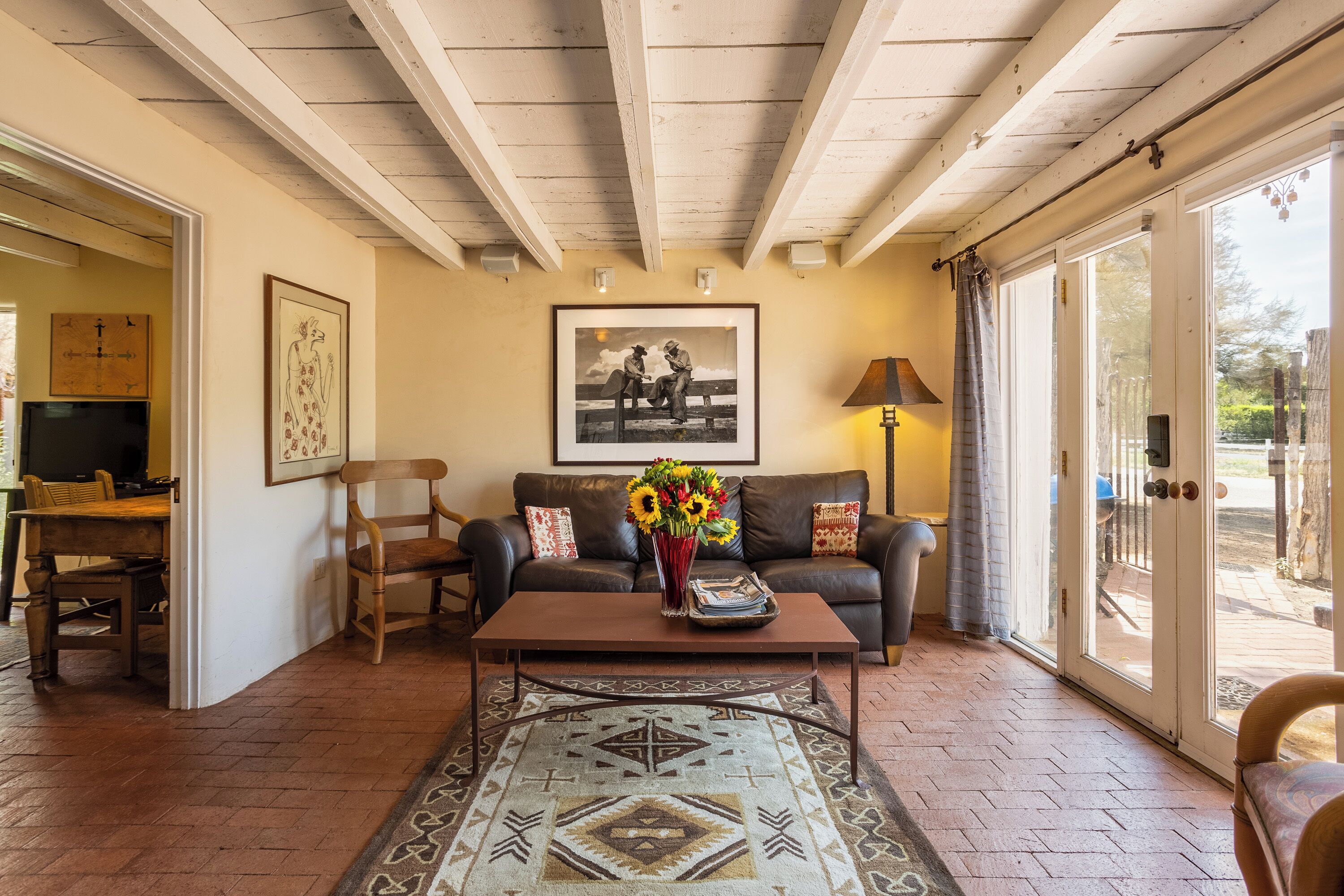 A living room with a brown leather sofa, a coffee table with a vase of flowers, a patterned rug, and a framed picture on the wall.