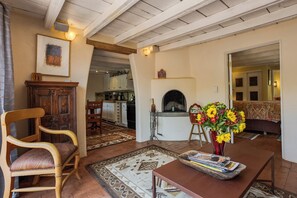 A living room with a wooden chair, a fireplace, a dining table with a vase of flowers, and a kitchen in the background. - Elegant Upscale Adobe Casita in Los Ranchos de Albuquerque District (Los Ranchos de Albuquerque)