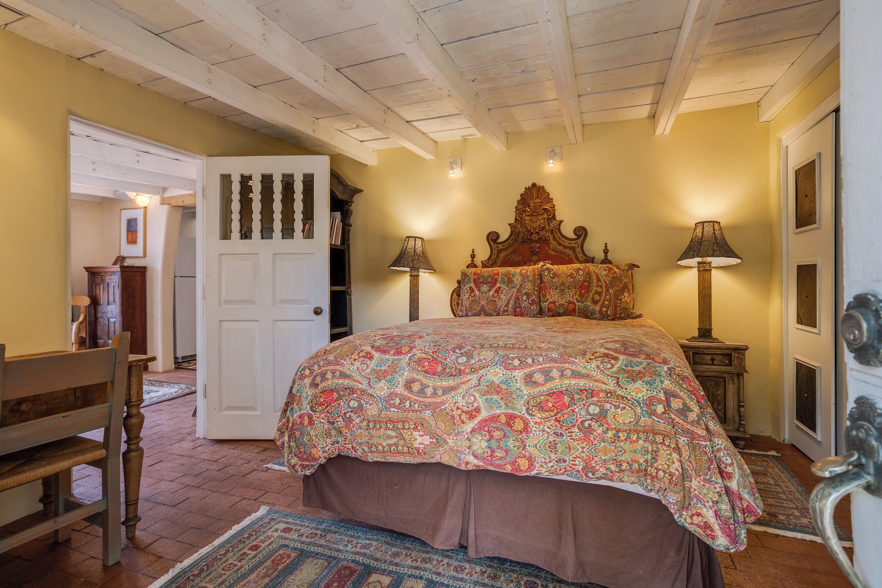 A bedroom with a large bed, two bedside lamps, a wooden headboard, a door, and a bench.