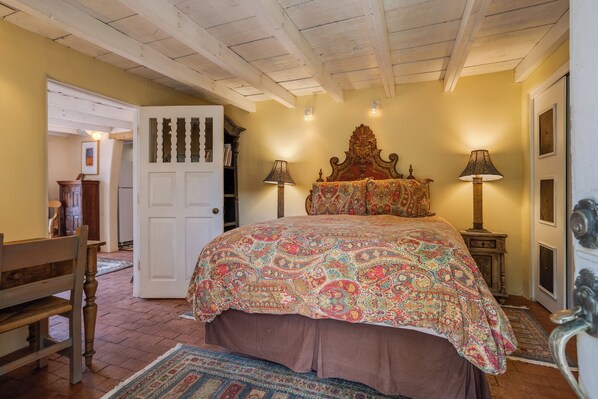 Quarto com cama grande, duas luminárias de cabeceira, cabeceira de madeira, uma porta e um banco.