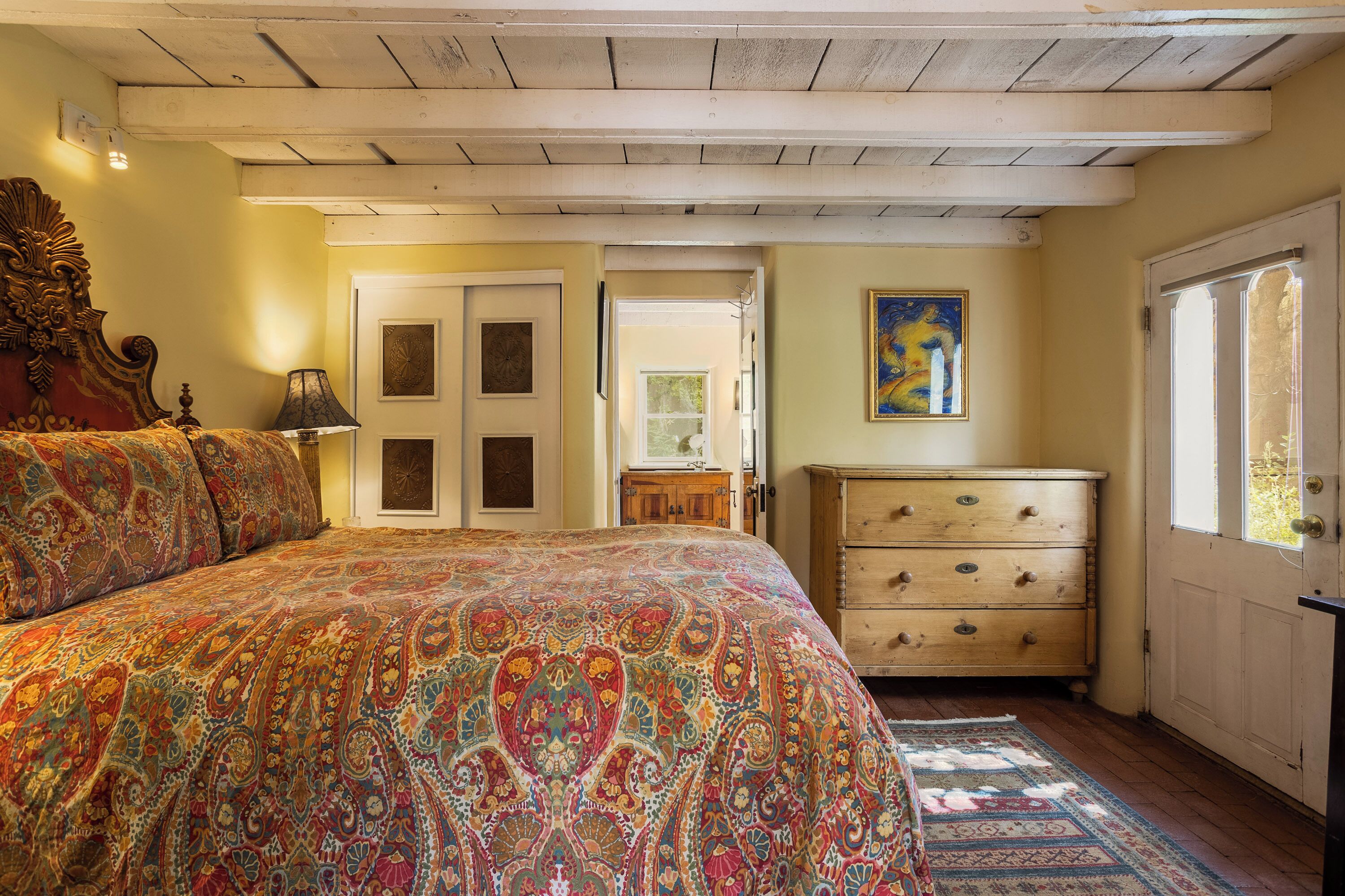 Une chambre à coucher avec un grand lit, une commode, une porte et un tableau accroché au mur.