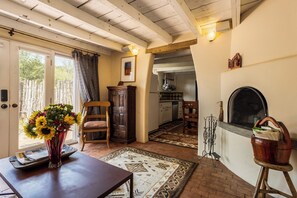 A room with a wooden table, a chair, a vase with flowers, a rug, a fireplace, and a kitchen area with hanging pots. - Elegant Upscale Adobe Casita in Los Ranchos de Albuquerque District (Los Ranchos de Albuquerque)