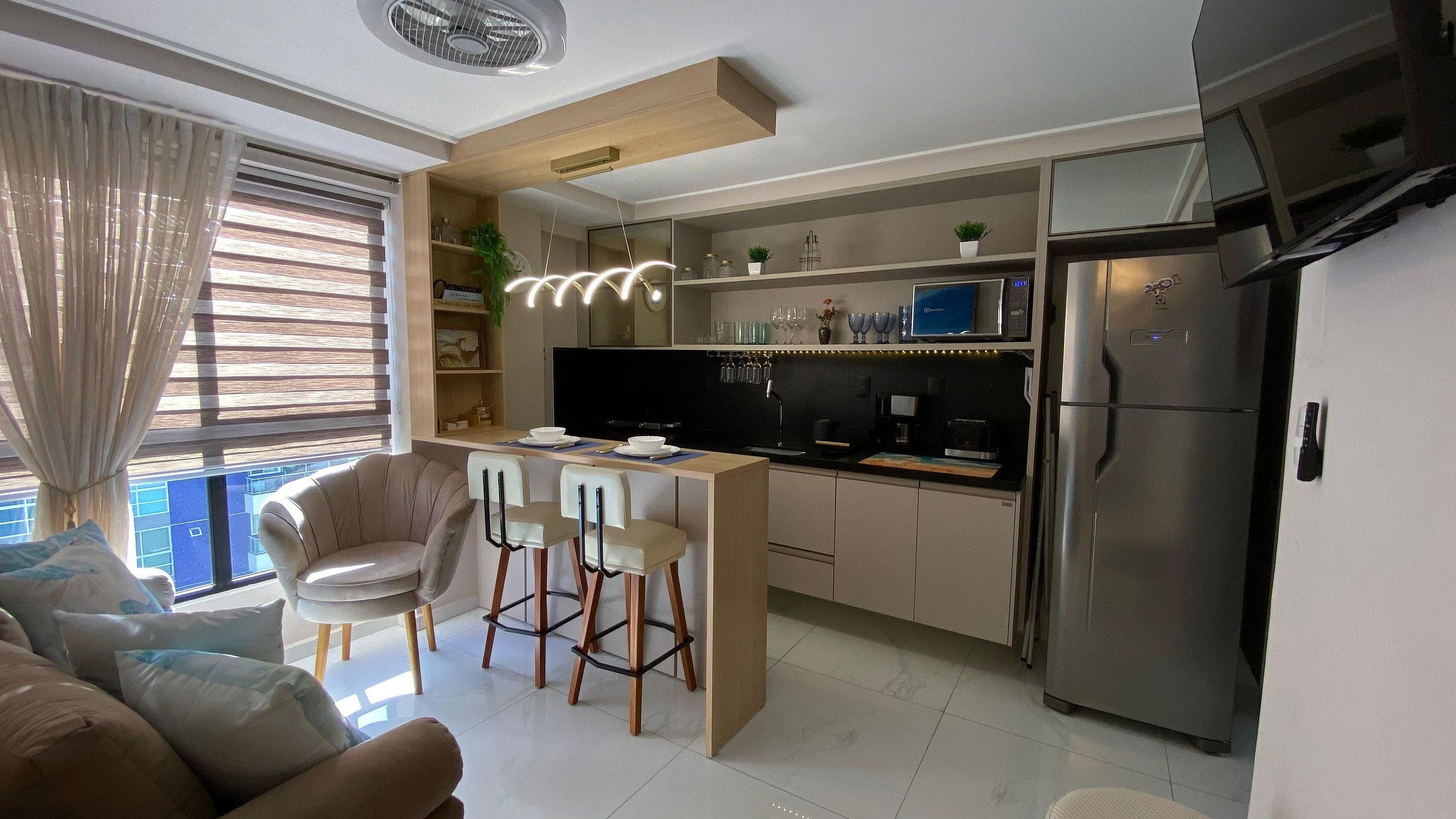 A modern kitchen with a central island, bar stools, a refrigerator, and a dining area with a sofa.