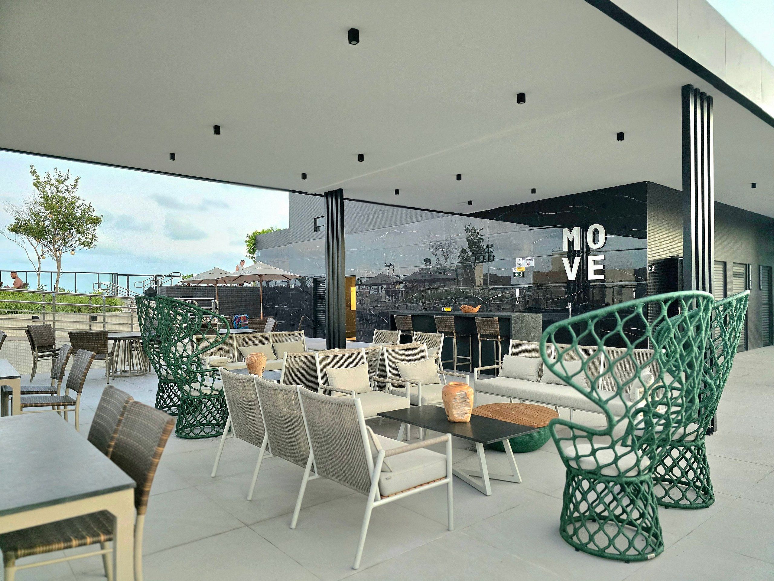 Un área de estar al aire libre con sillas y mesas de mimbre, una zona de bar con mostrador, y vistas al mar.