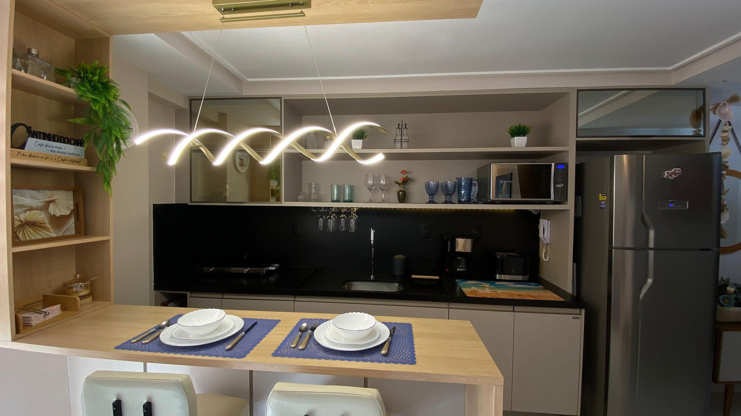 A modern kitchen with a dining table set for two, a microwave, a refrigerator, and a hanging light fixture.