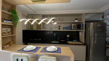 A modern kitchen with a dining table set for two, a microwave, a refrigerator, and a hanging light fixture.