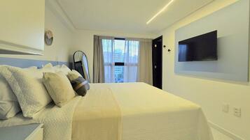 A hotel room with a bed, a flat-screen TV mounted on the wall, and a window with curtains.