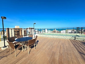 A rooftop terrace with a round table and wicker chairs, overlooking a cityscape and the sea. - Move By Hosppedar (João Pessoa)