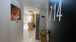 A hallway with a number sign, a painting, and a plant. - Move By Hosppedar (João Pessoa)