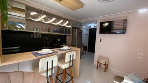 Una cocina moderna con barra, una mesa de comedor con sillas, un refrigerador, un microondas y un televisor montado en la pared.