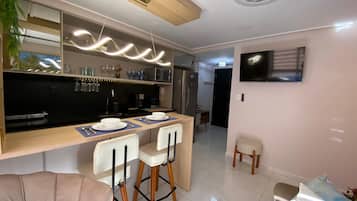 Una cucina moderna con angolo bar, un tavolo da pranzo con sedie, un frigorifero, un forno a microonde e una TV a parete.