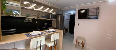 Une cuisine moderne avec un coin bar, une table à manger avec des chaises, un réfrigérateur, un four à micro-ondes et un téléviseur fixé au mur.