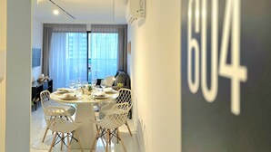 Un comedor moderno con una mesa redonda para cuatro personas, sillas blancas y un gran ventanal con cortinas.