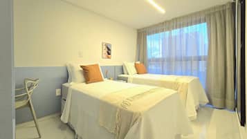 Camera d'albergo con due letti, una sedia, una finestra con tende e un quadro appeso al muro.