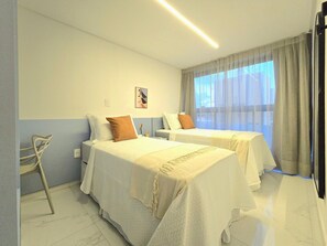 Camera d'albergo con due letti, una sedia, una finestra con tende e un quadro appeso al muro.