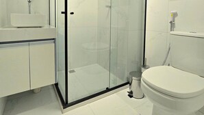 Un baño moderno con ducha envuelta en vidrio, inodoro, lavamanos con espejo y repisa con artículos de aseo.