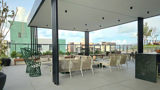 Un patio al aire libre con asientos y mesas, rodeado de plantas en macetas y vistas a un paisaje urbano.