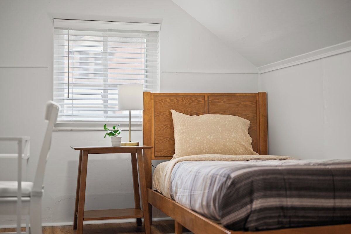 Une chambre à coucher avec un lit en bois, une table de chevet avec une lampe et une fenêtre avec des stores.