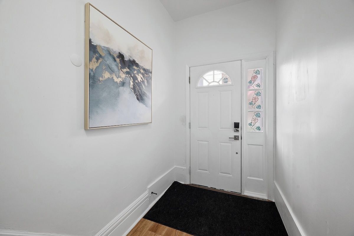 Um corredor com uma porta branca, um tapete de entrada preto e um quadro abstrato emoldurado na parede.