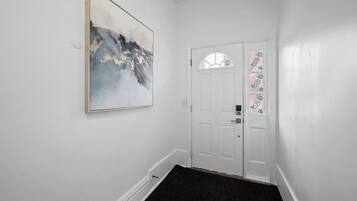 Um corredor com uma porta branca, um tapete de entrada preto e um quadro abstrato emoldurado na parede.