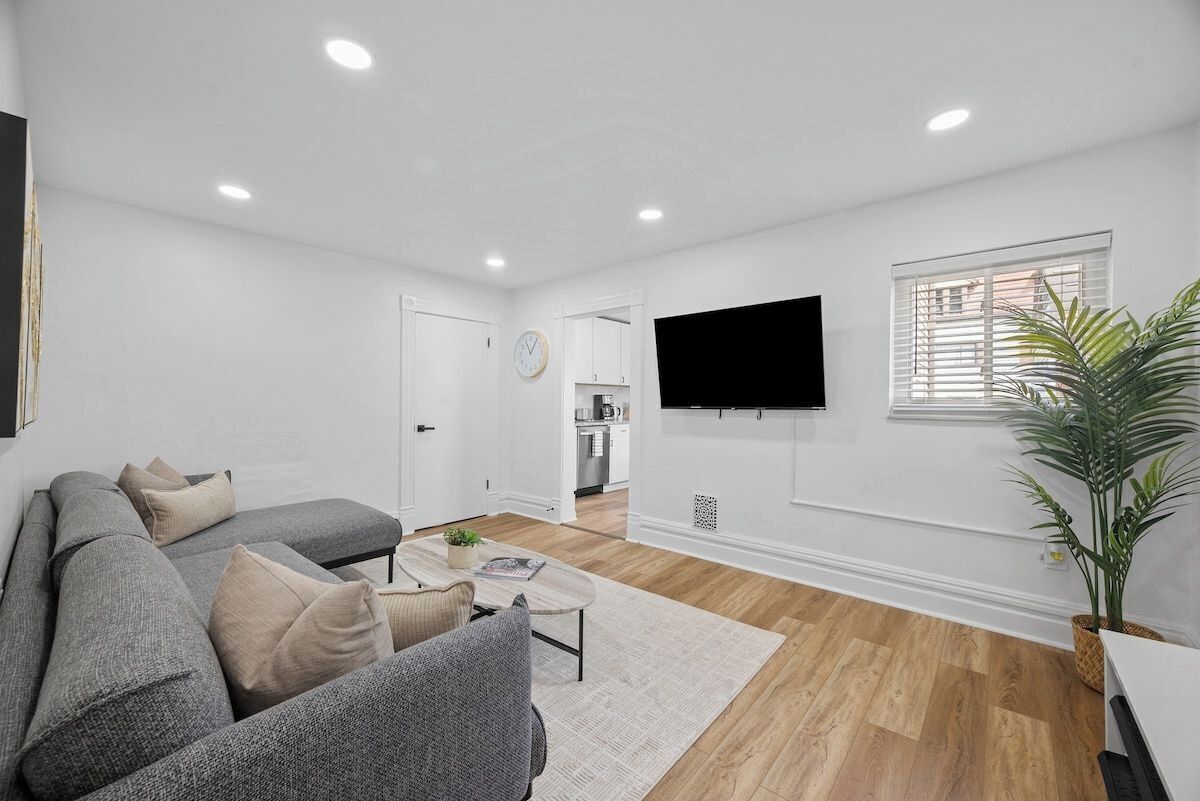 Uma sala de estar moderna com um sofá seccional cinza, uma mesa de centro e uma televisão de tela plana na parede.