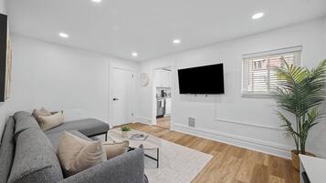 Uma sala de estar moderna com um sofá seccional cinza, uma mesa de centro e uma televisão de tela plana na parede.