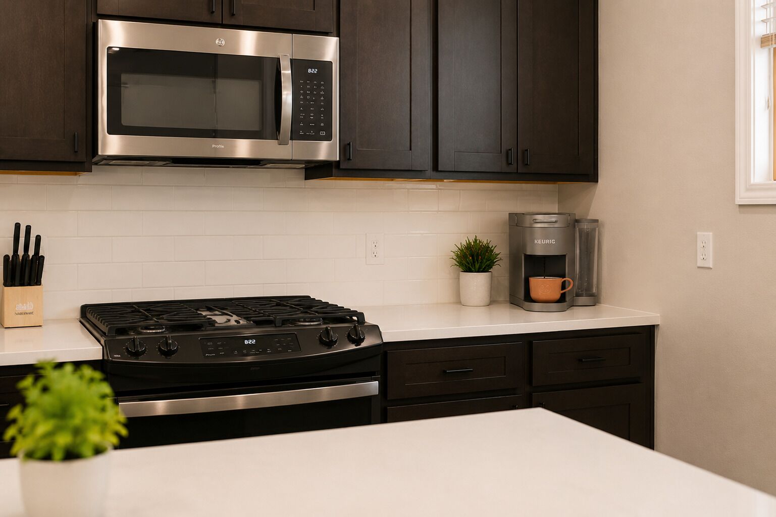 A modern kitchen with dark cabinets, a stainless steel microwave, a gas stove, and a coffee maker.