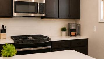 A modern kitchen with dark cabinets, a stainless steel microwave, a gas stove, and a coffee maker.