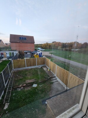 A residential backyard with a wooden fence, a brick house, and a paved driveway. - The Walnut (South Ockendon)