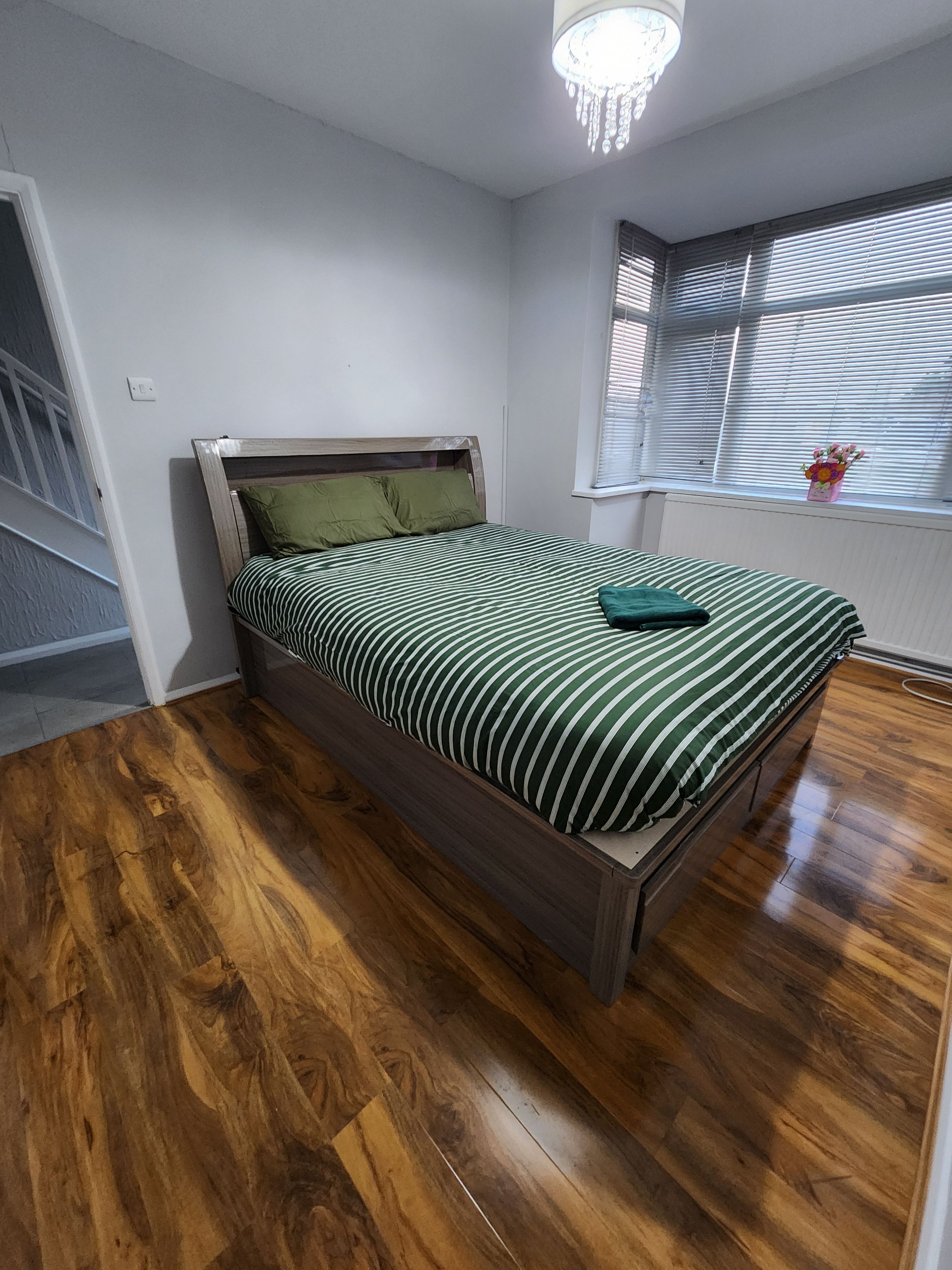 Un dormitorio con cama de madera, una ventana con persianas y una araña.