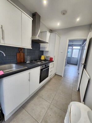 A kitchen with white cabinets, a black countertop, a stove, and a sink. - The Walnut (South Ockendon)