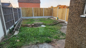 A backyard with a wooden fence, a brick house, and a concrete path.