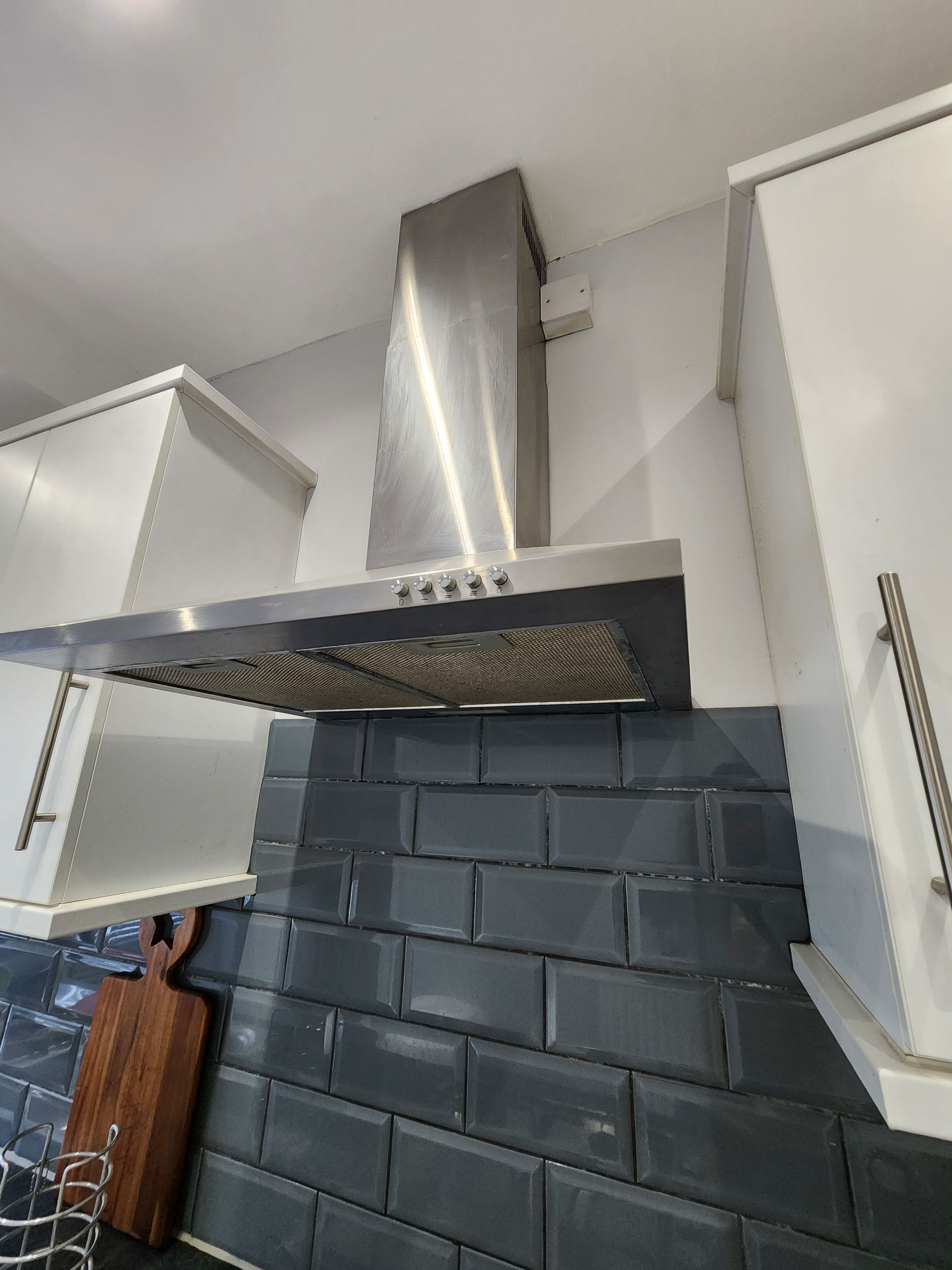 A kitchen with a stainless steel range hood, white cabinets, and a black tiled backsplash.