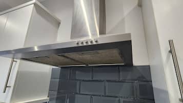 A kitchen with a stainless steel range hood, white cabinets, and a black tiled backsplash.