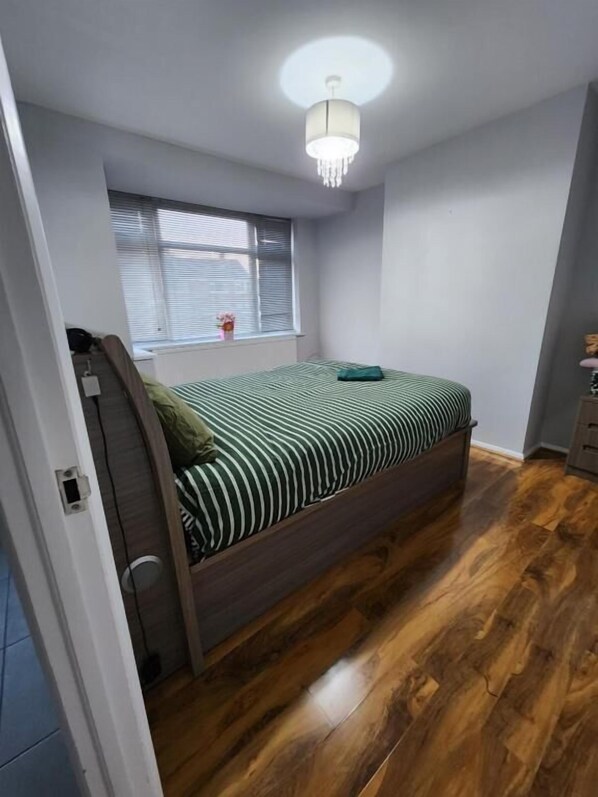 A bedroom with a bed, a window, and a wooden floor. - The Walnut (South Ockendon)