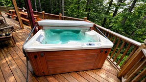 Un jacuzzi en una terraza de madera rodeado de árboles.