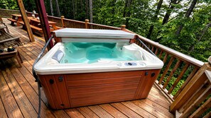 Ein Whirlpool auf einer Holzterrasse, umgeben von Bäumen.