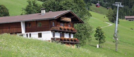 A traditional chalet with a sloped roof, wooden balconies with flower boxes, and a view of a ski lift in the background.