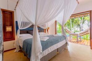 A bedroom with a bed, white canopy, wooden headboard, and a view of the outdoors. - Paraíso Casa Branca (Arraial d'Ajuda)